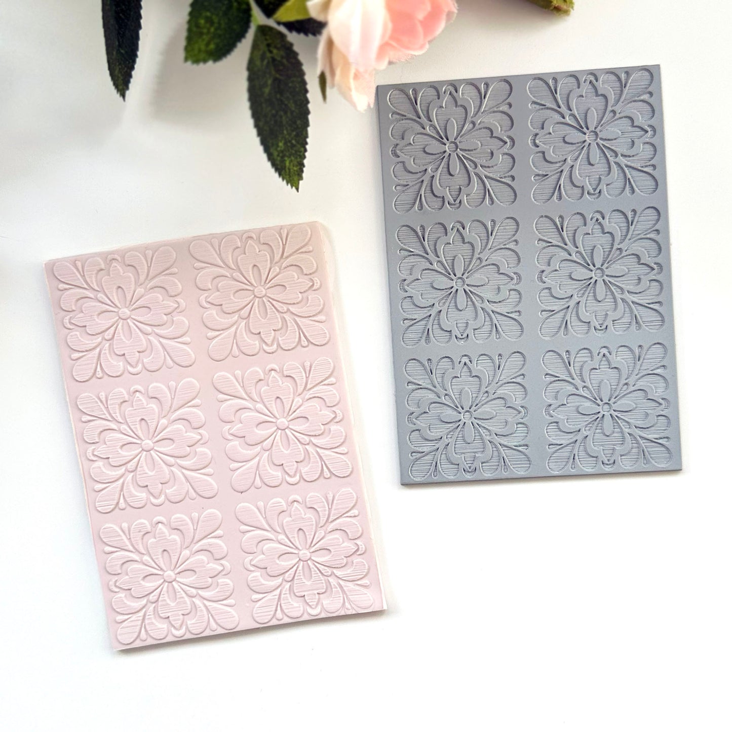 Pale pink rectangular  sheet of polymer clay with embossed floral motifs of portuguese spanish tiles with a gray rubber texture sheet placed behind it on a white surface. Decorative leaves and a flower are partially visible at the top.