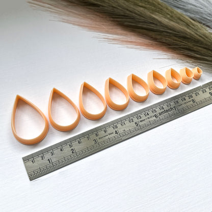 A set of nine peach-coloured plastic clay cutters in various sizes, ranging from 10mm to 50mm. The cutters are shaped like raindrops and have a ruler under them for size comparison.