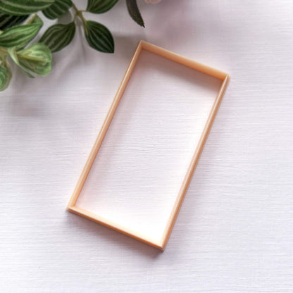 A rectangular clay cutter in a light peach , photographed on a white textured surface with green leaves in the top-left corner.