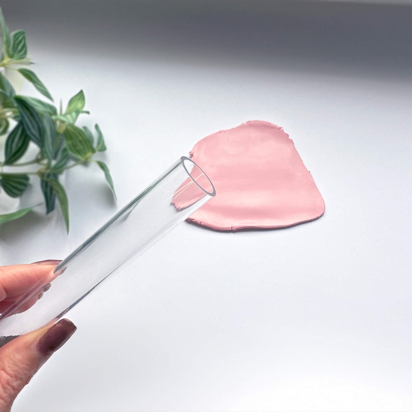 Clear hollow acrylic rolling pin with pink clay on a light gray background