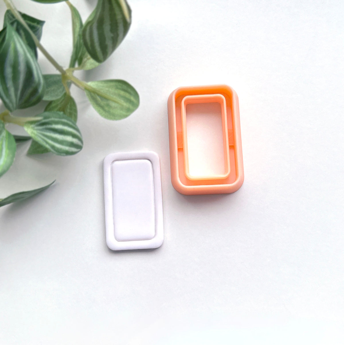 Rounded rectangle clay cutter sits on a white background next to a white polymer cut out made using the cutter.