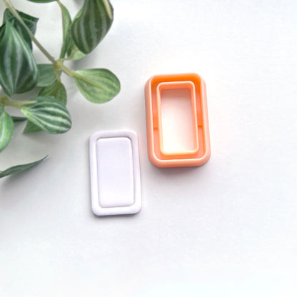 Rounded rectangle clay cutter sits on a white background next to a white polymer cut out made using the cutter.