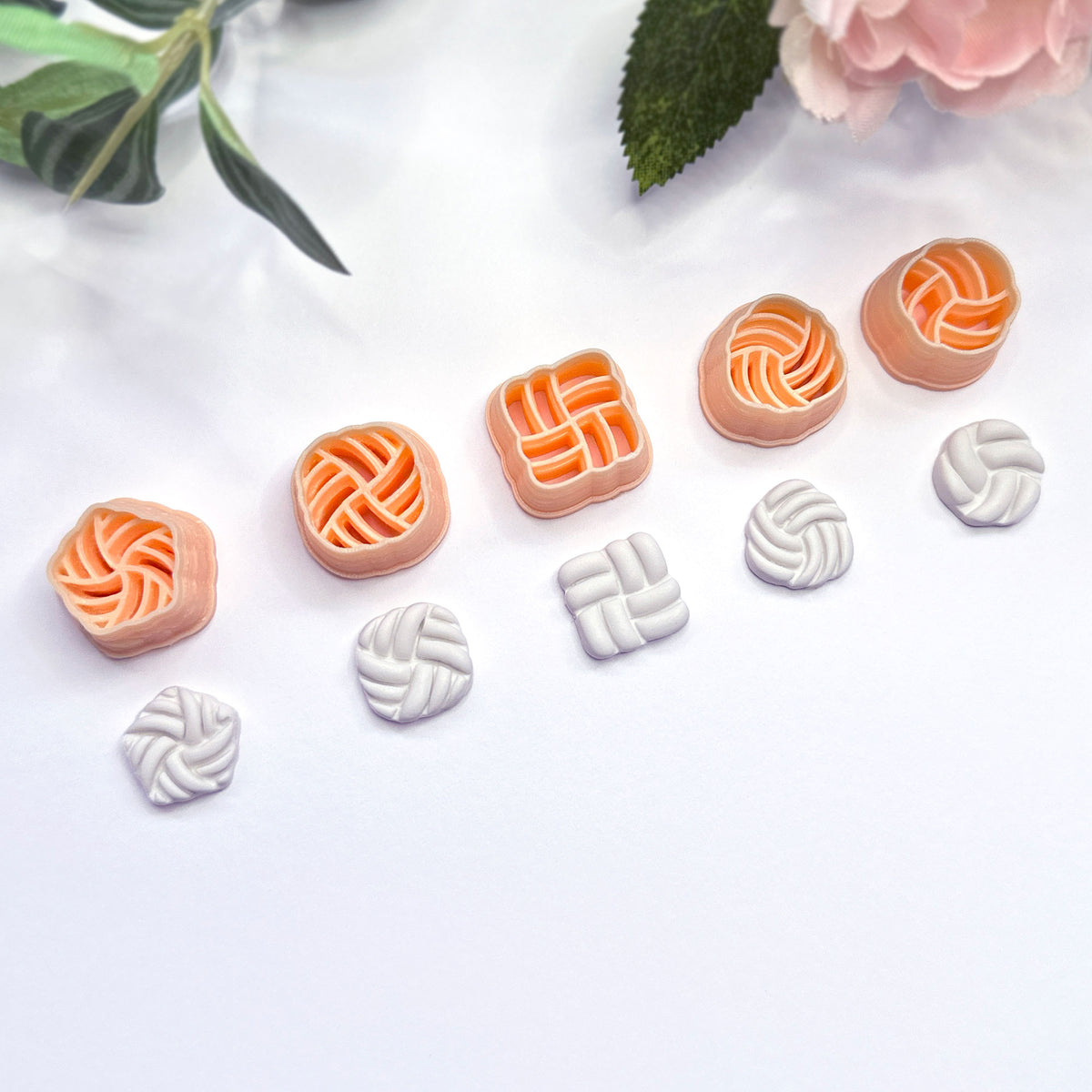 Five peach-colored knot-shaped polymer clay cutters are arranged on a white surface, with five matching white clay pieces shown below each cutter. Green leaves and a pink flower appear as decorative props in the top corners.