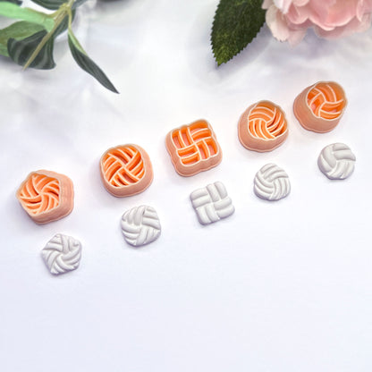 Five peach-colored knot-shaped polymer clay cutters are arranged on a white surface, with five matching white clay pieces shown below each cutter. Green leaves and a pink flower appear as decorative props in the top corners.