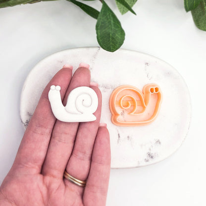 hand holding white snail shaped polymer clay cut out- snail in shell clay cutter