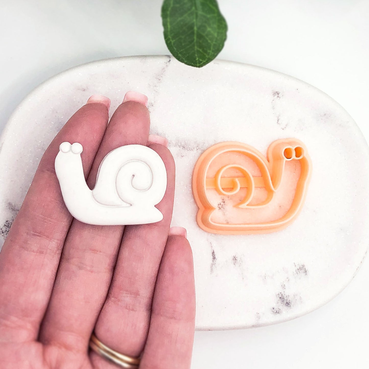hand holding white snail shaped polymer clay cut out- snail in shell clay cutter
