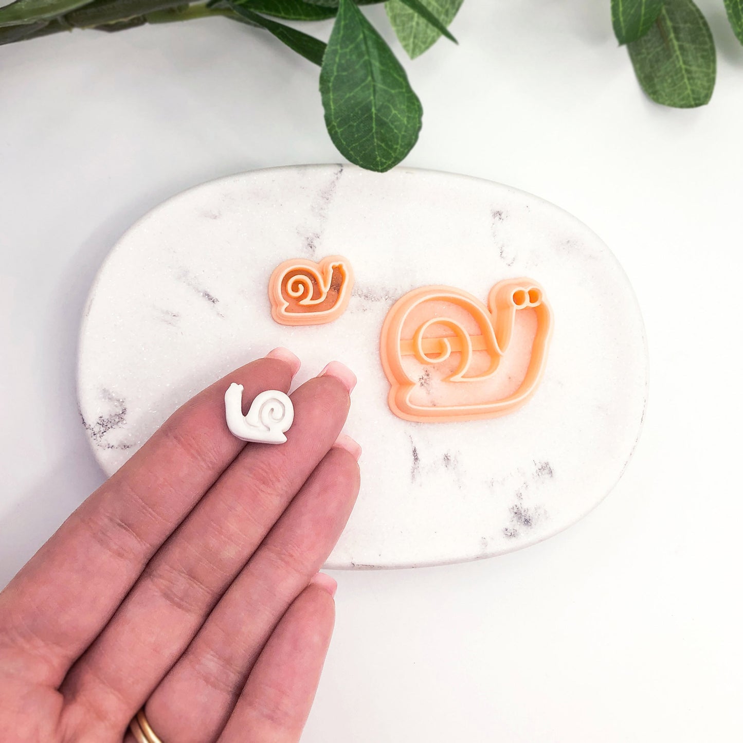 hand holding white snail shaped polymer clay cut out- snail in shell clay cutter