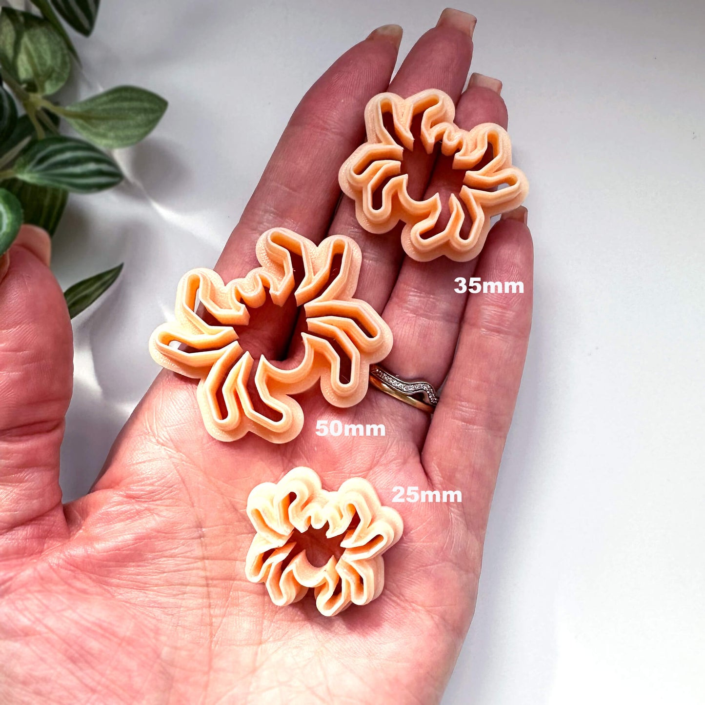 Three spider-shaped cookie clay cutters in peach are displayed on a person's hand to show scale, with size labels '25mm', '35mm', and '50mm' overlaid on the image.