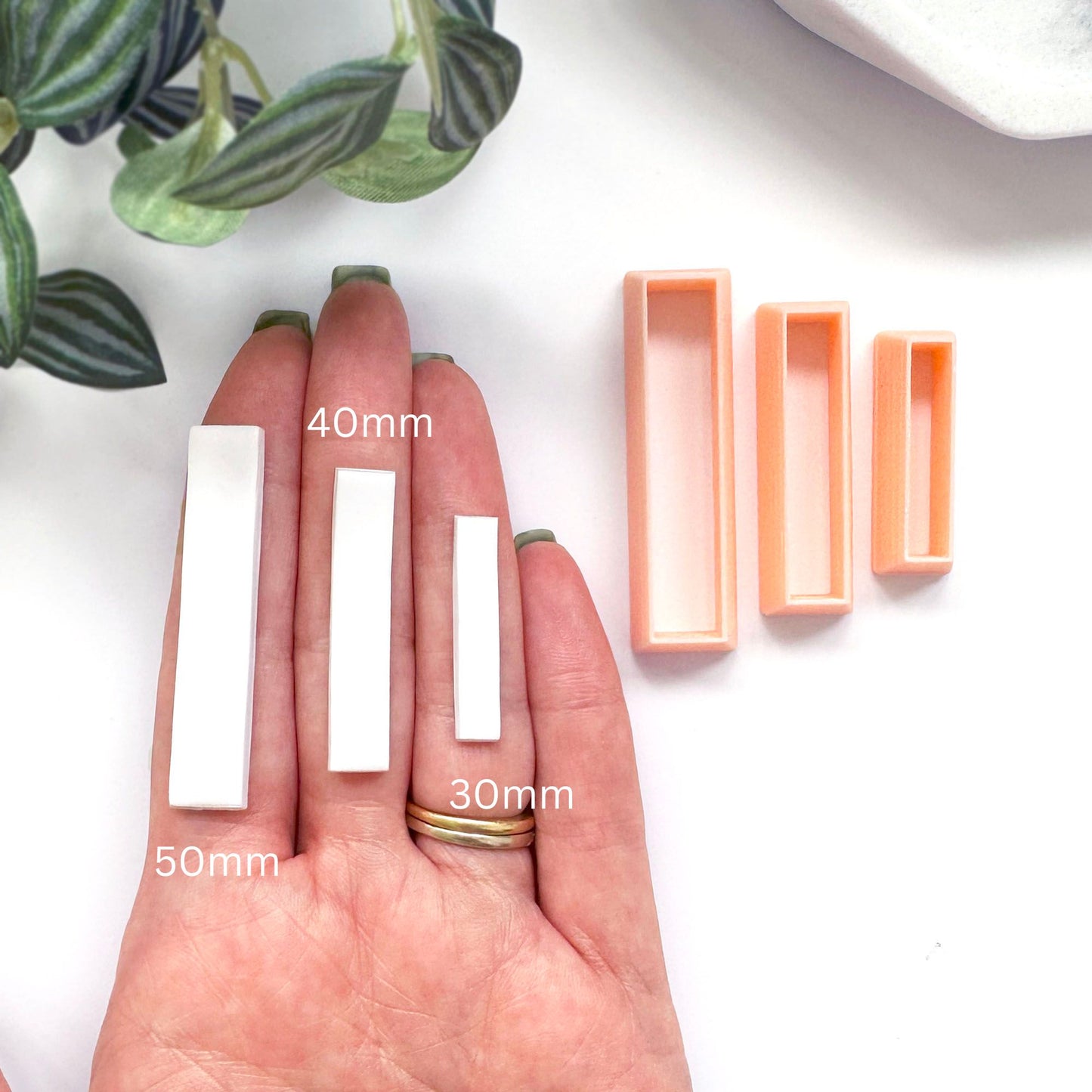 A hand displays three white rectangular polymer clay bars in 50mm, 40mm, 30mm, and peach-colored empty rectangular molds, with size labels overlaid on the image against a white background with a plant leaf in the corner.