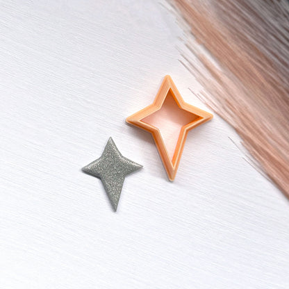 A small glittery star-shaped clay cutout next to a star-shaped cookie clay cutters on a light surface.