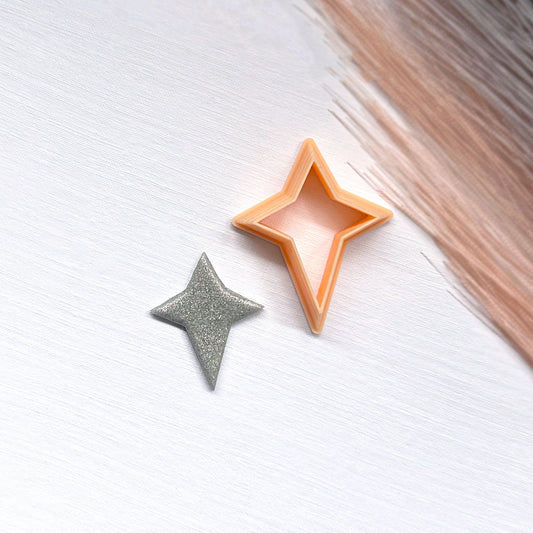 A small glittery star-shaped clay cutout next to a star-shaped cookie clay cutters on a light surface.