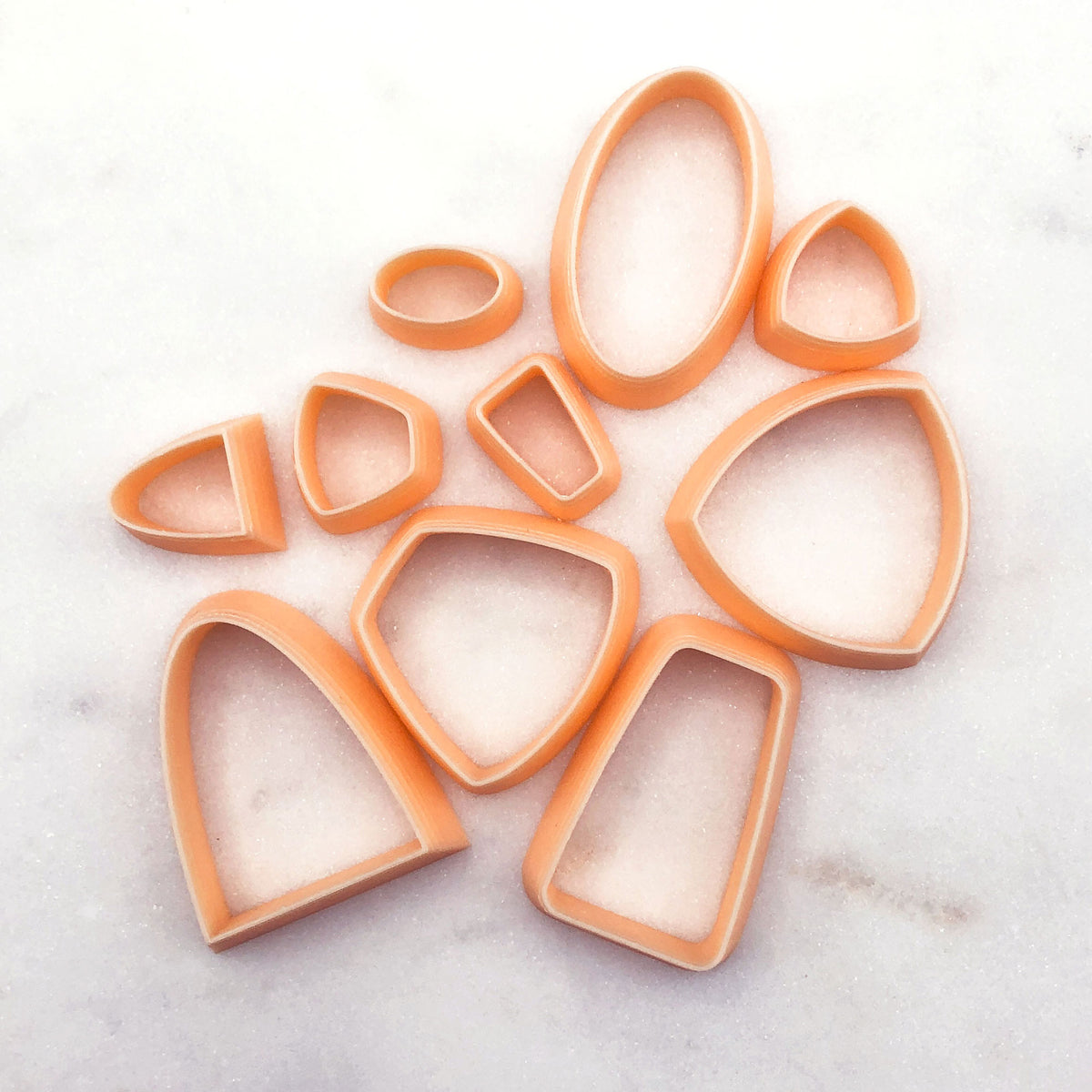 A set of peach-colored plastic clay cookie cutters in various shapes, arranged on a light gray marble surface.