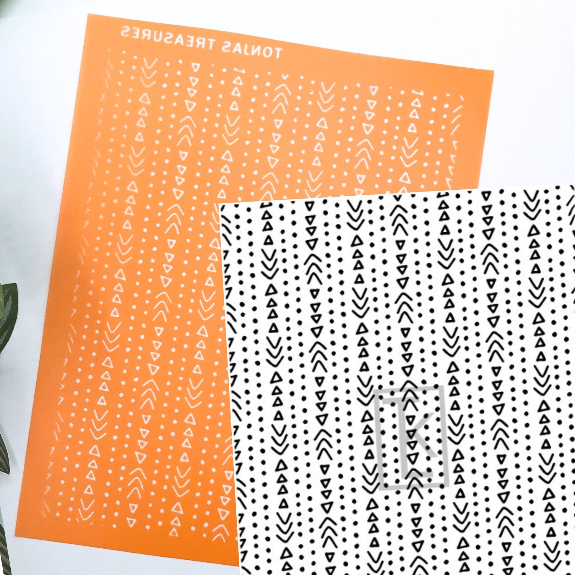 Two patterned silkscreens displayed on a white background. One sheet is bright orange with white vertical rows of small dots, triangles, and arrow-like marks, and the other is white with black matching vertical pattern rows.