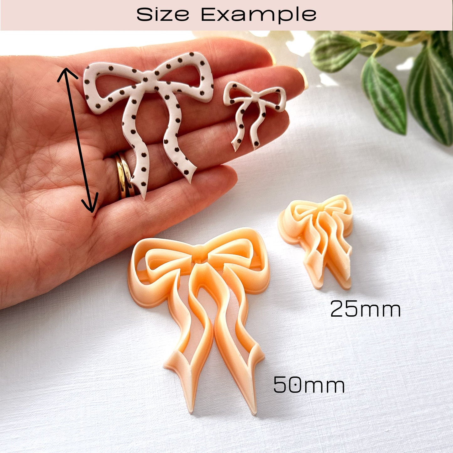 Hand holding bow-shaped polymer clay cut-outs on a light surface with the clay cutters in the front and a plant in the background - size examples