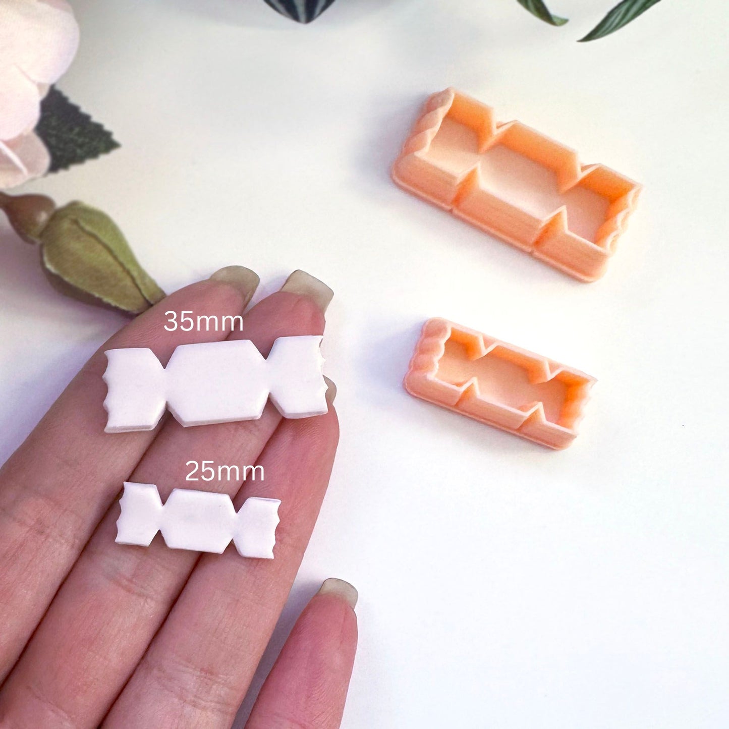 A hand holds two small white sweet-shaped pieces next to two peach-colored plastic cookie cutters, with size labels '35mm' and '25mm' overlaid on the image.