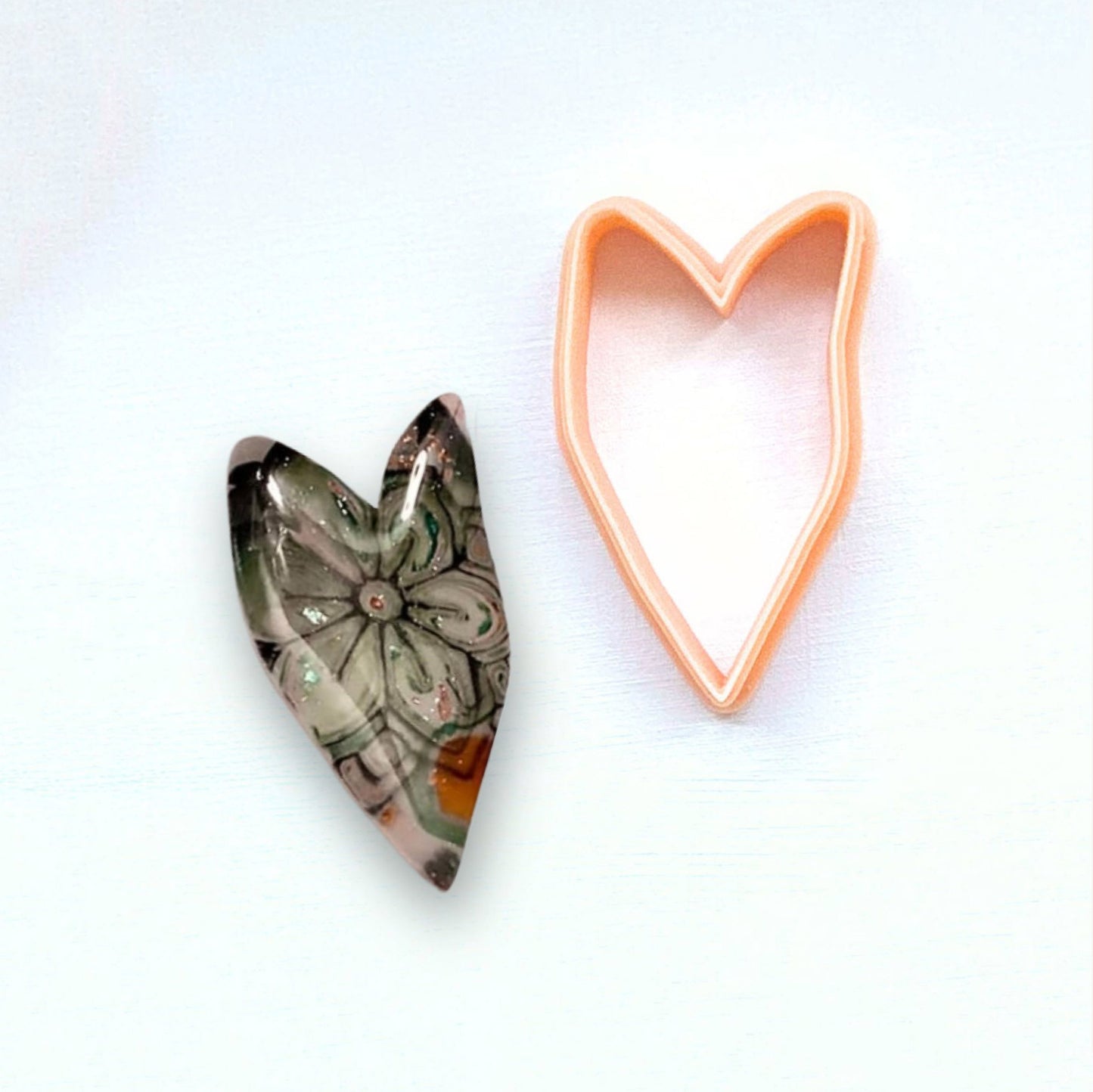 Heart-shaped clay cutter next to a heart-shaped polymer clay piece on a white background - organic cookie cutter