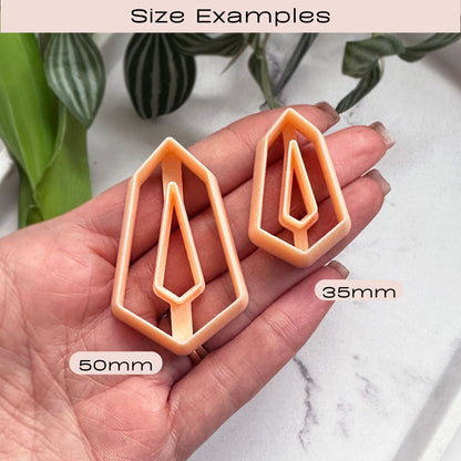 Two geometric crystal-inspired cookie clay cutters held in a hand with size labels on a marble surface.