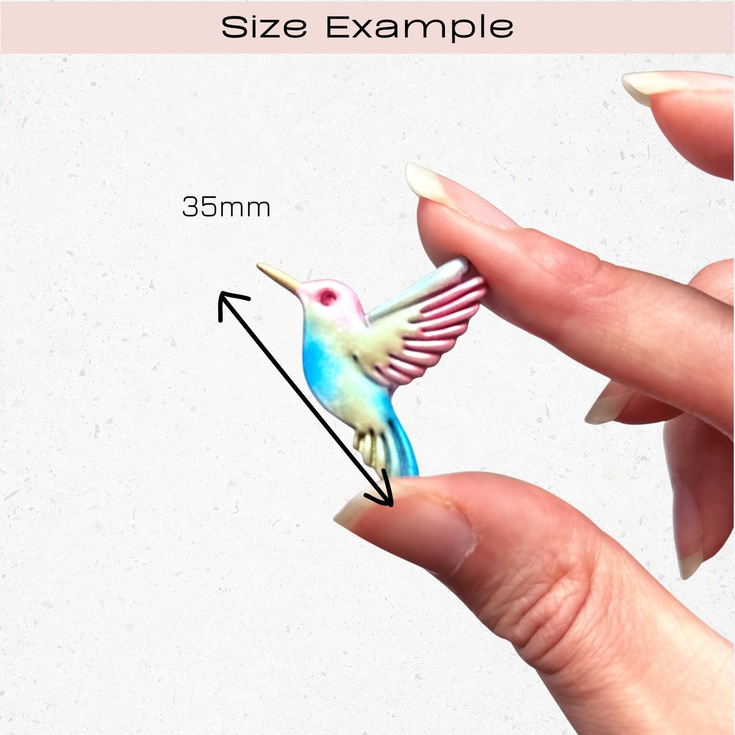 Colorful hummingbird figurine held between fingers with a measurement label indicating 35mm.