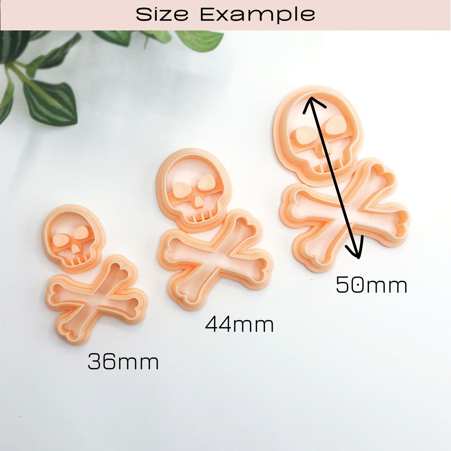Three peach-colored skull and crossbones cookie cutters shown on a white background with size labels and arrows indicating 36mm, 44mm, and 50mm. A pink header at the top reads 'Size Example'.