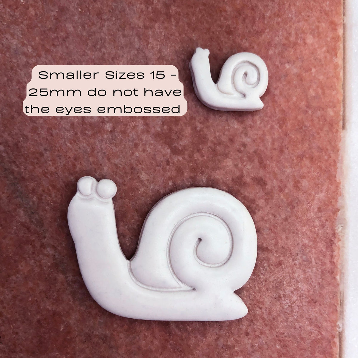 hand holding white snail shaped polymer clay cut out- snail in shell clay cutter - photo writing states that smaller sizes 15-25mm do not have eyes embossed