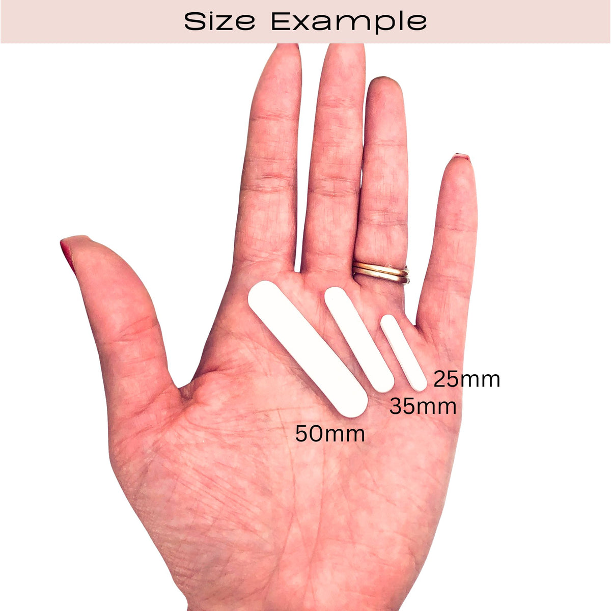 A hand shown palm-up with three white oval capsule clay cut outs of different sizes placed on the palm, labeled 50mm, 35mm, and 25mm, under the heading 'Size Example'.