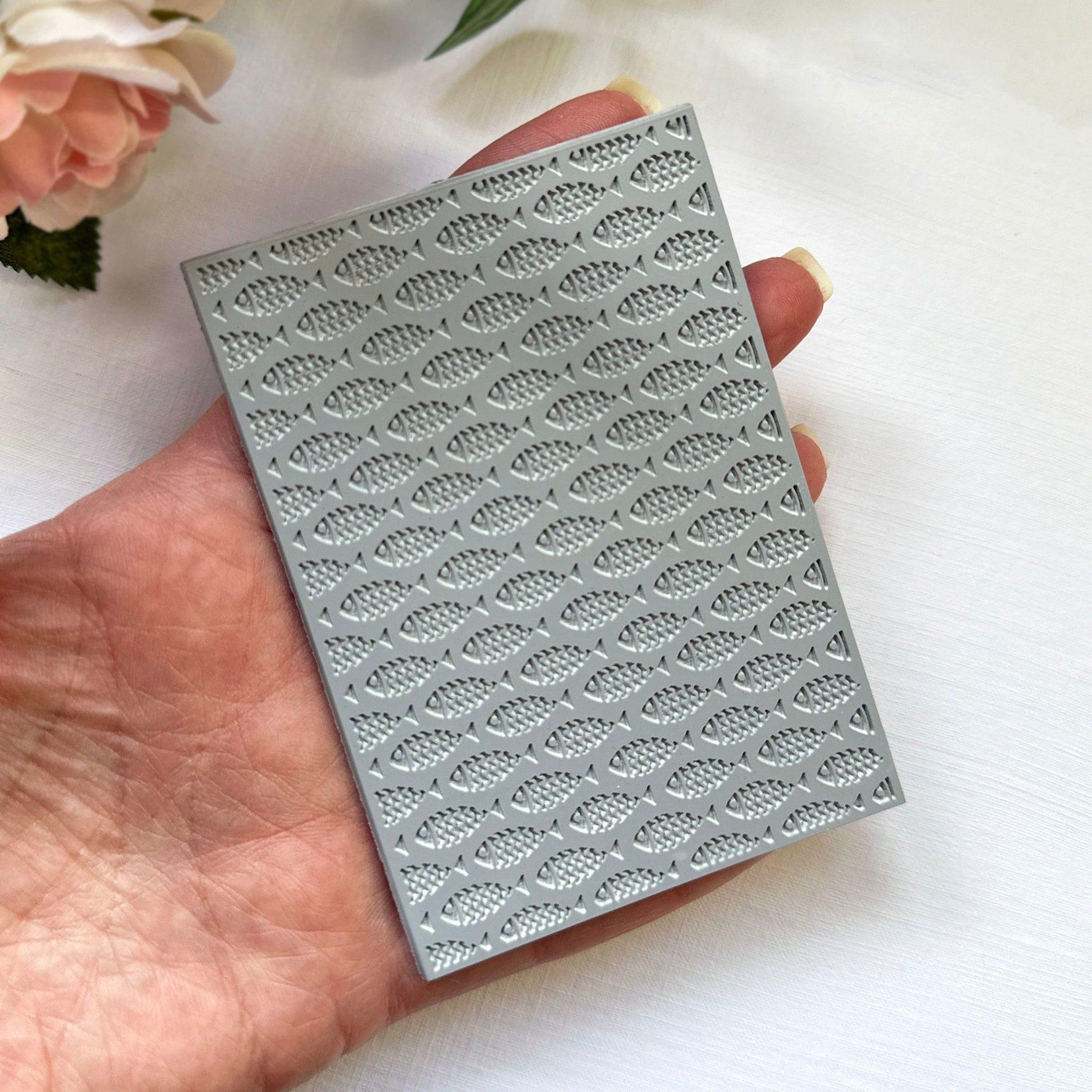 Hand holding a texture stamp with a school-of-fish print against a light background with flowers.