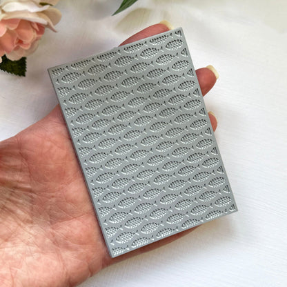 Hand holding a texture stamp with a school-of-fish print against a light background with flowers.