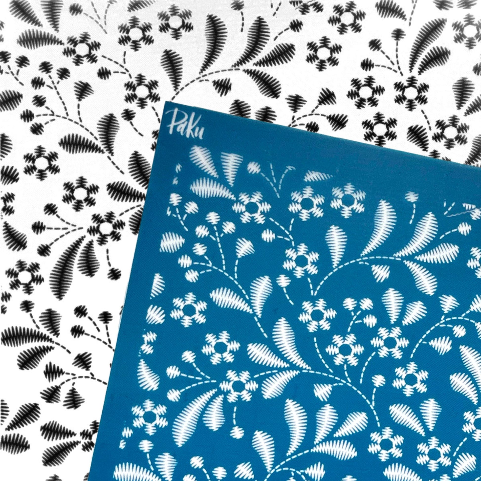 A blue stencilled silkscreen sheet with a white floral and leaf pattern, placed diagonally over a white background featuring the same black-and-white floral print.