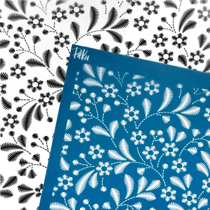 A blue stencilled silkscreen sheet with a white floral and leaf pattern, placed diagonally over a white background featuring the same black-and-white floral print.