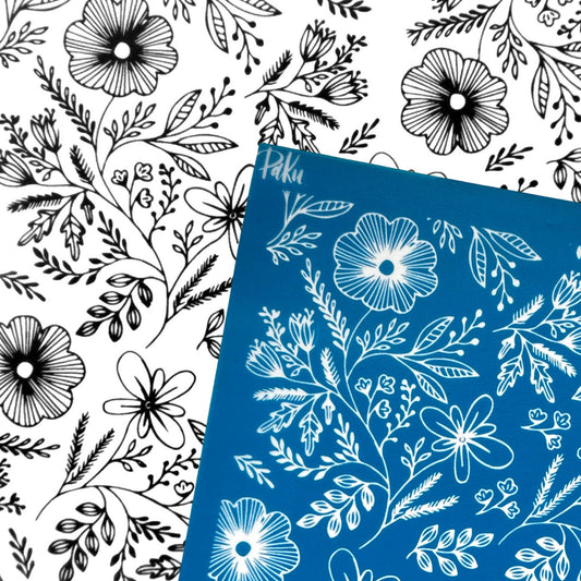 A blue rectangular silkscreen stencil with a white floral line-art pattern, placed diagonally over a white background covered in the same black floral line-art pattern.