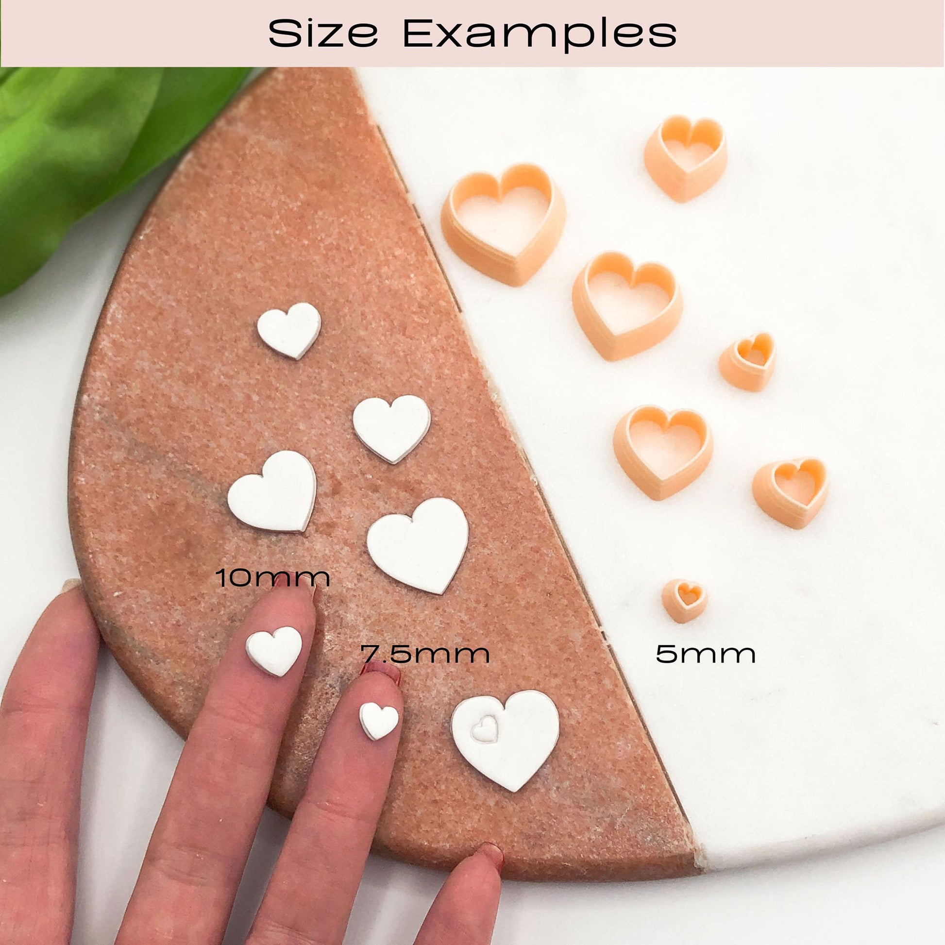Heart-shaped cookie clay cutters shown in size examples on a split white and brown surface, with a hand holding a 10mm cutter and text labels reading 10mm, 7.5mm, and 5mm.