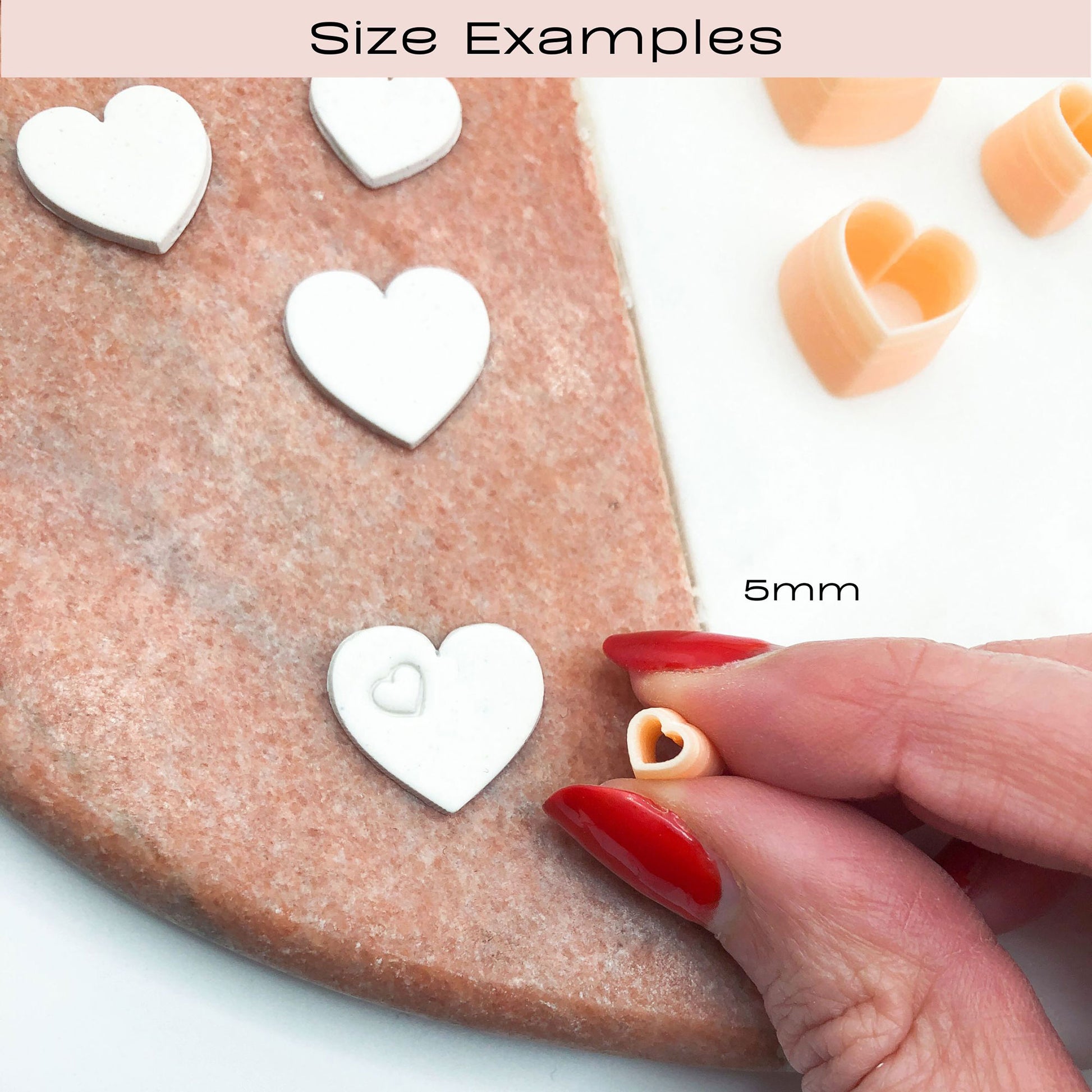 Size examples of heart-shaped craft cutters or stamps, showing larger white hearts on a pink surface and a hand holding a small peach-colored heart piece. Text labels indicate 5mm size.
