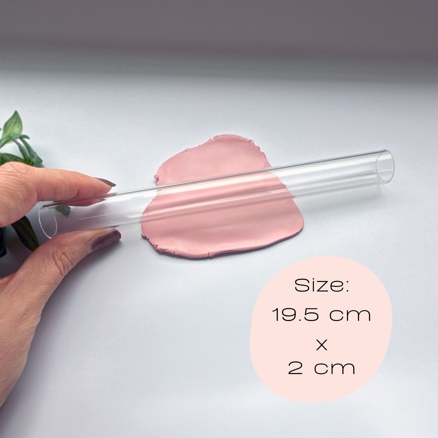 Clear hollow acrylic rolling pin held by a hand with pink clay on a light gray background