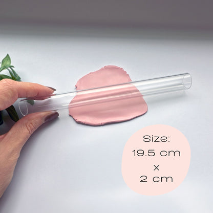 Clear hollow acrylic rolling pin held by a hand with pink clay on a light gray background