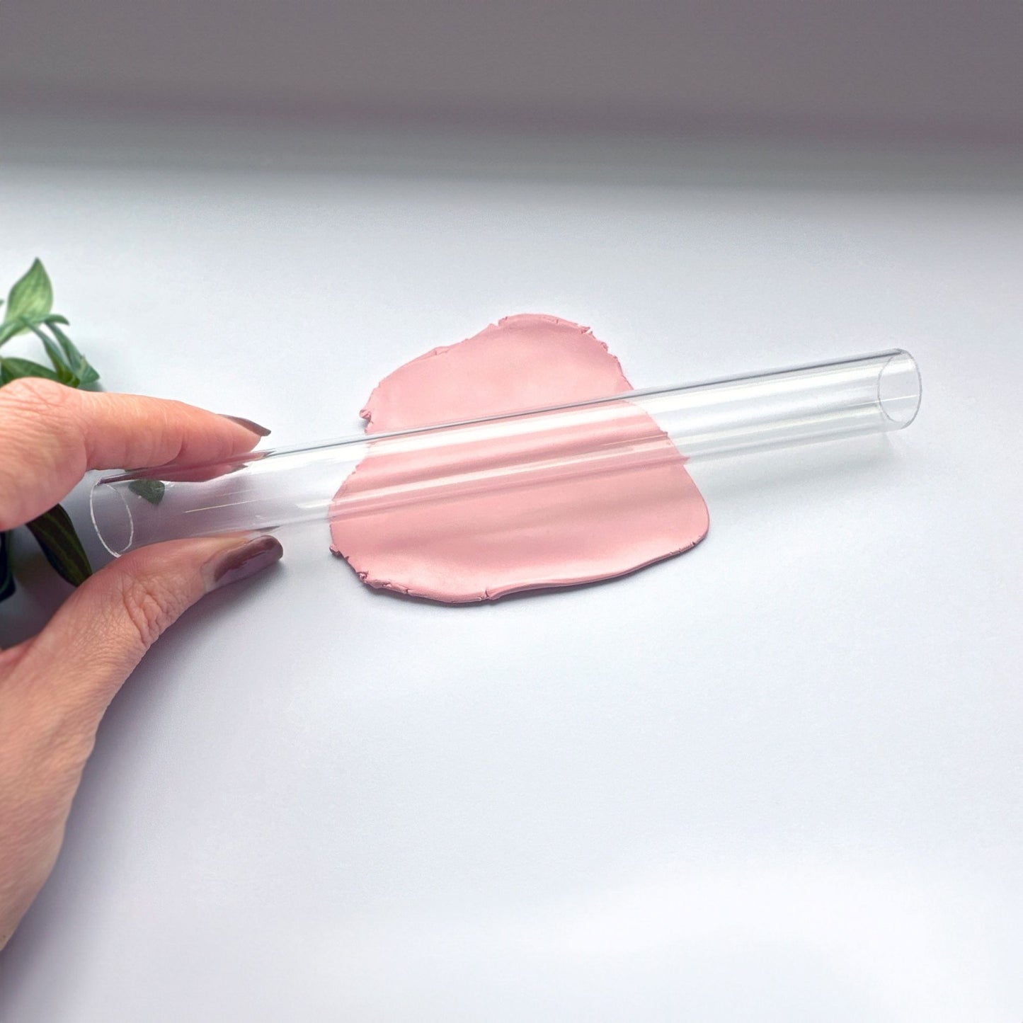 Clearhollow acrylic rolling pin held by a hand with pink clay on a white background