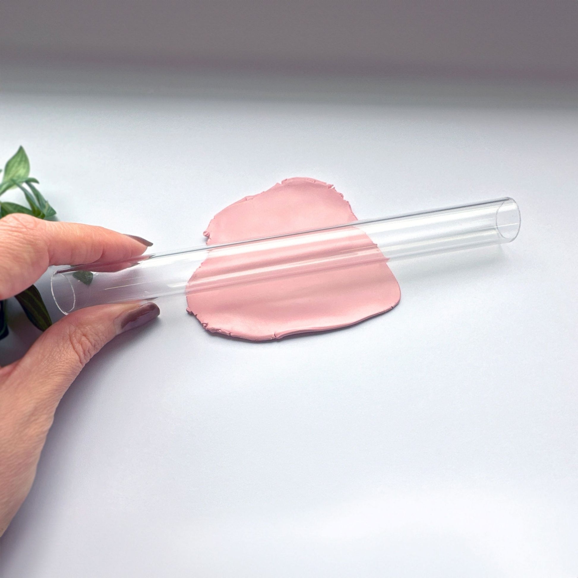 Clearhollow acrylic rolling pin held by a hand with pink clay on a white background