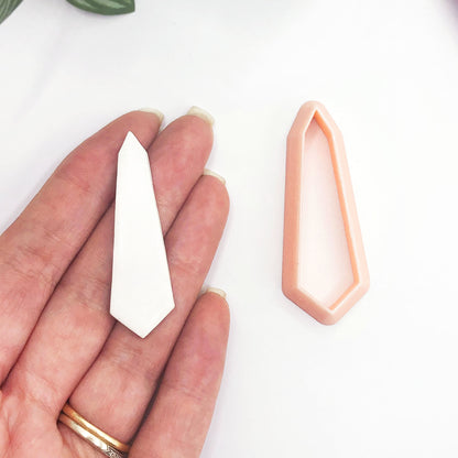 A hand holds a small white geometric crystal-shaped piece next to a peach-colored cutter on a clean white background.