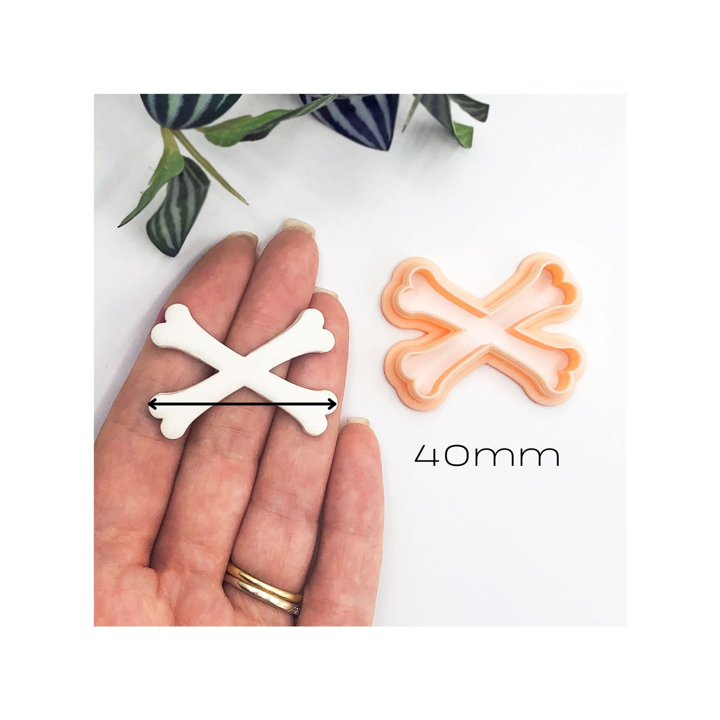 A peach plastic cookie clay cutter in the shape of crossed bones. The cutter is shown next to a white clay piece that has been cut out using the cutter.