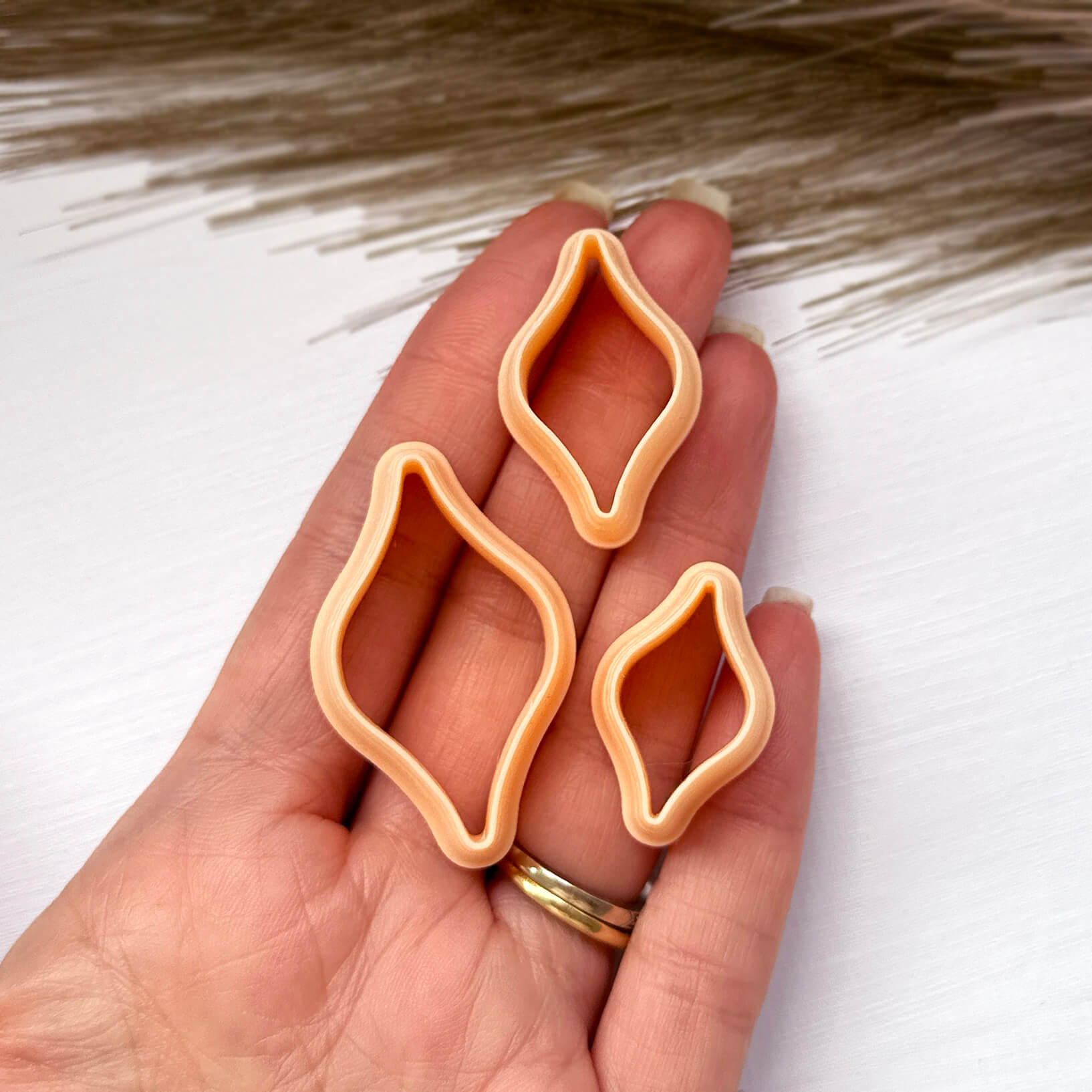 Three peach-colored, ogee bulb-shaped cookie cutters held in a person's hand against a white background with dried grass.