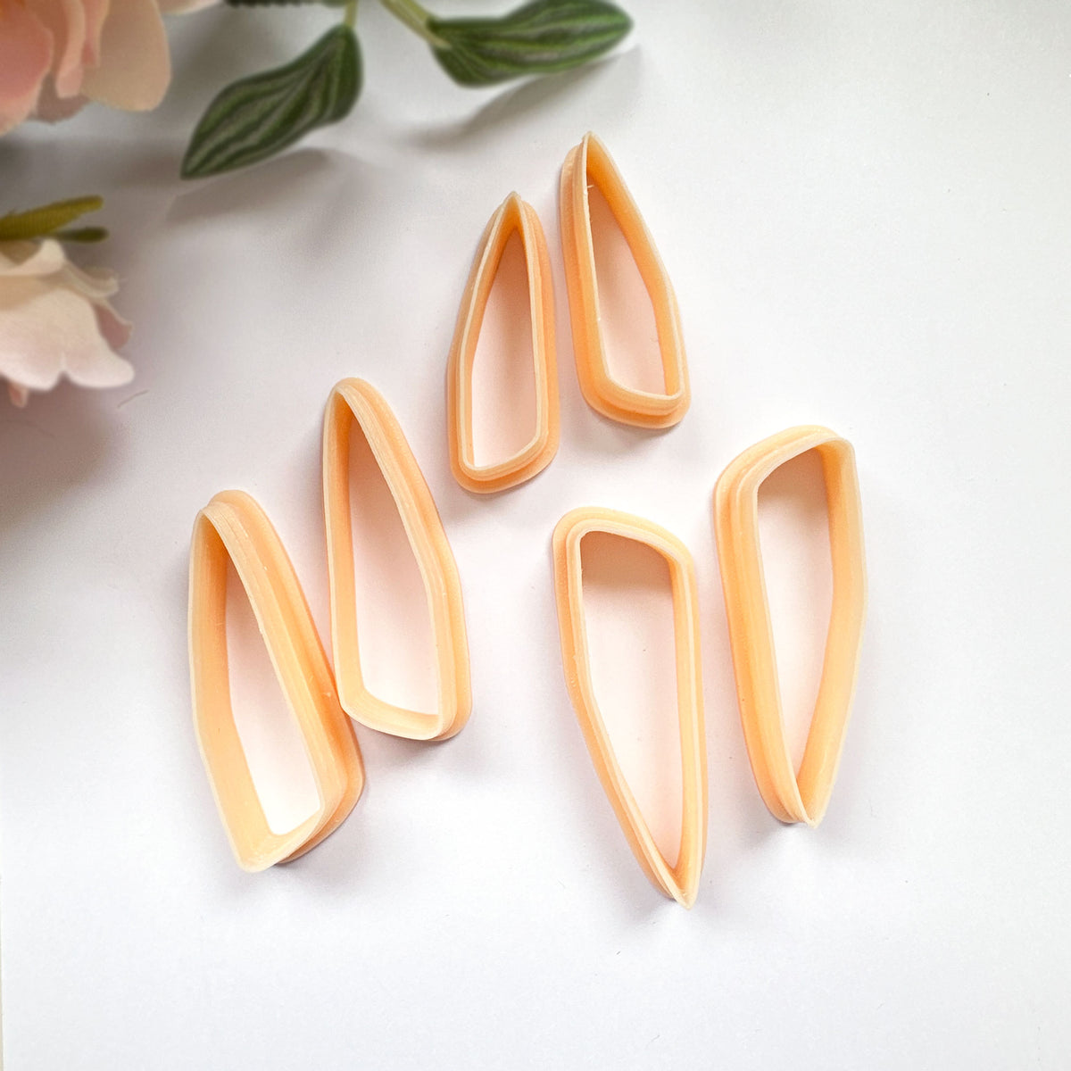 Clayboutique organic scalene dagger peach clay cutter mirror set of two in three sizes on a white back ground with flowers in the corner