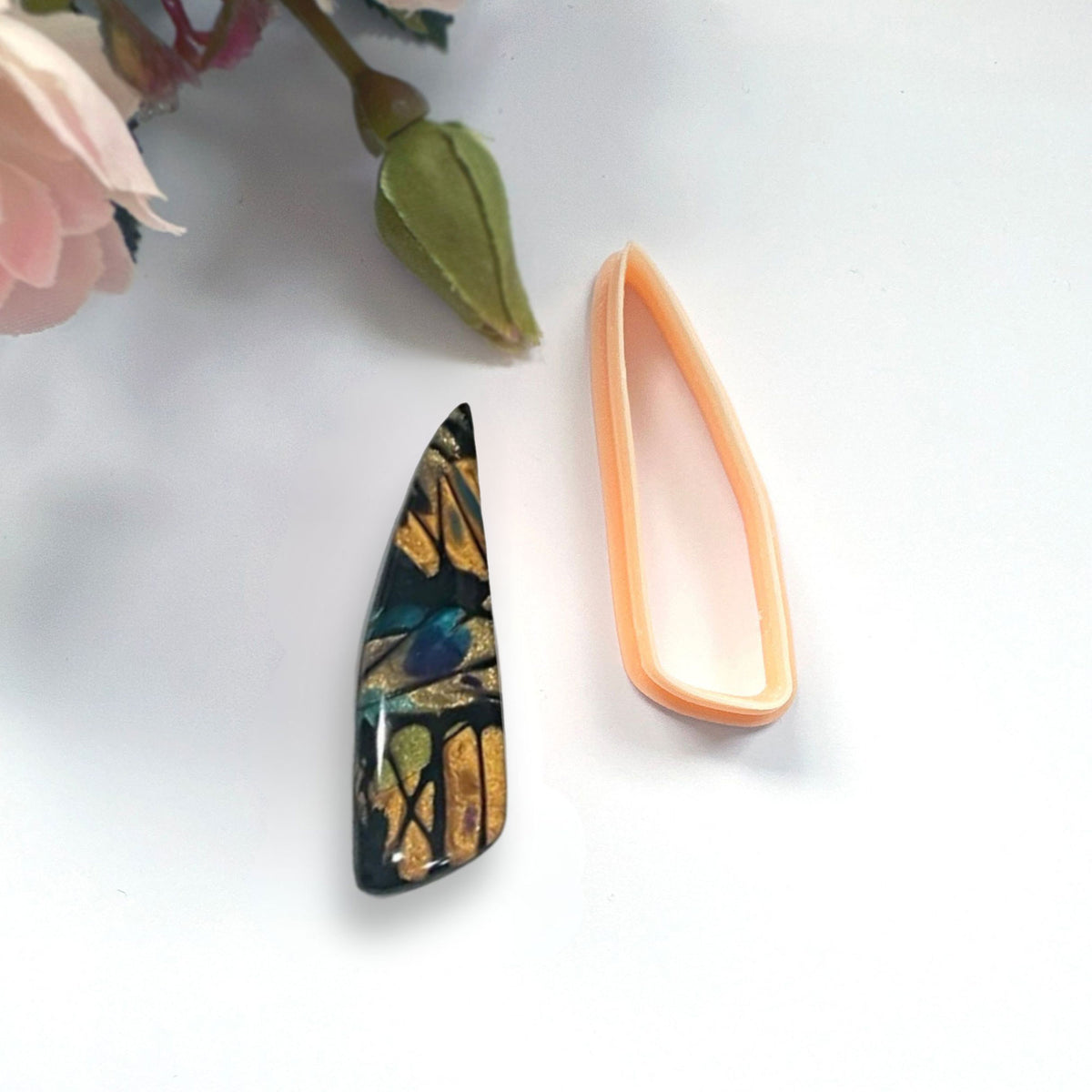 Clayboutique organic scalene dagger peach clay cutter shown next to a finished polymer clay cut out bead of the shape.
