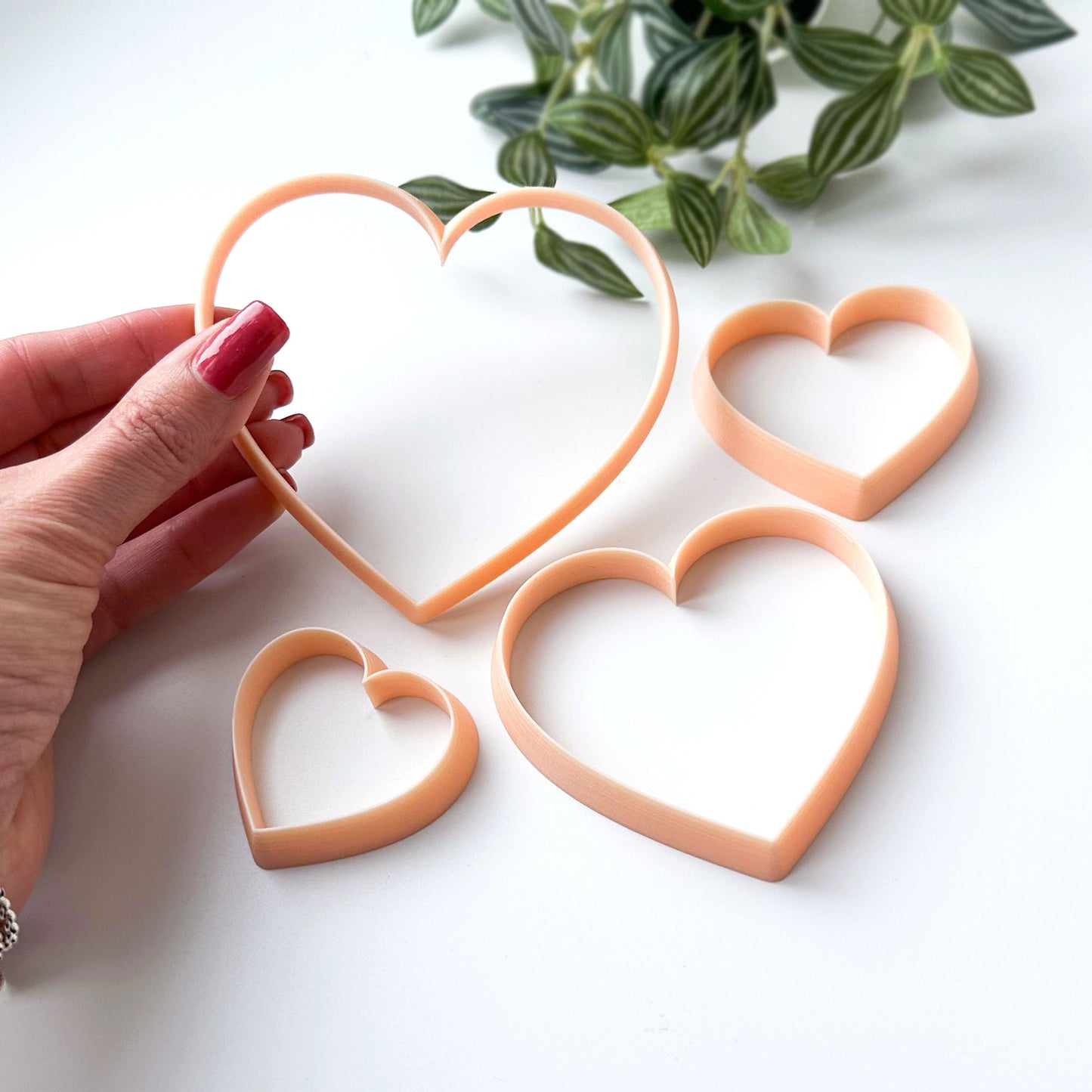Heart-shaped cookie cutters on a white surface with a hand holding one of them.