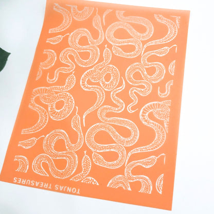 An orange rectangular silkscreen stencil featuring a repeating white snake pattern and the text 'TONIAS TREASURES' along the bottom edge, photographed on a white background.