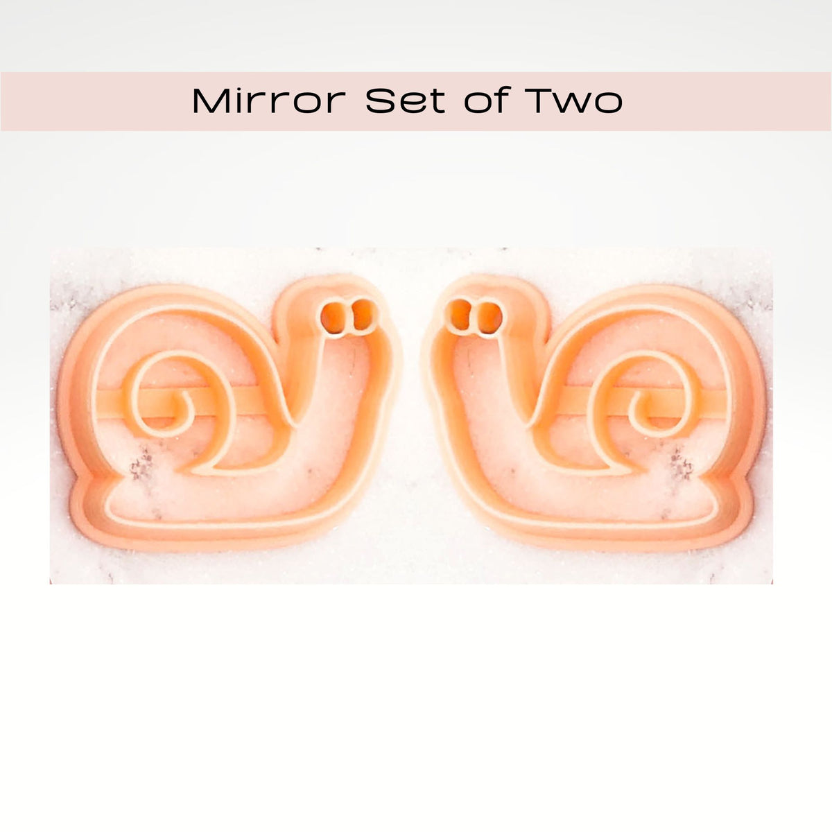 Two matching peach-colored snail-shaped cookie cutters shown side by side on a white marble surface, with a pale pink banner at the top reading 'Mirror Set of Two'.