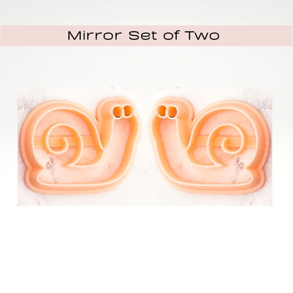 Two matching peach-colored snail-shaped cookie cutters shown side by side on a white marble surface, with a pale pink banner at the top reading 'Mirror Set of Two'.