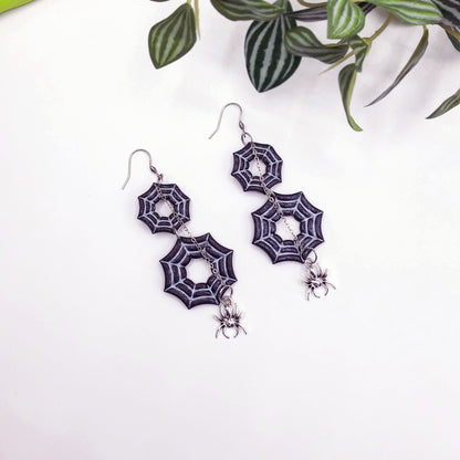 Polymer clay Spider web earrings with spider charms on a white background with green leaves.