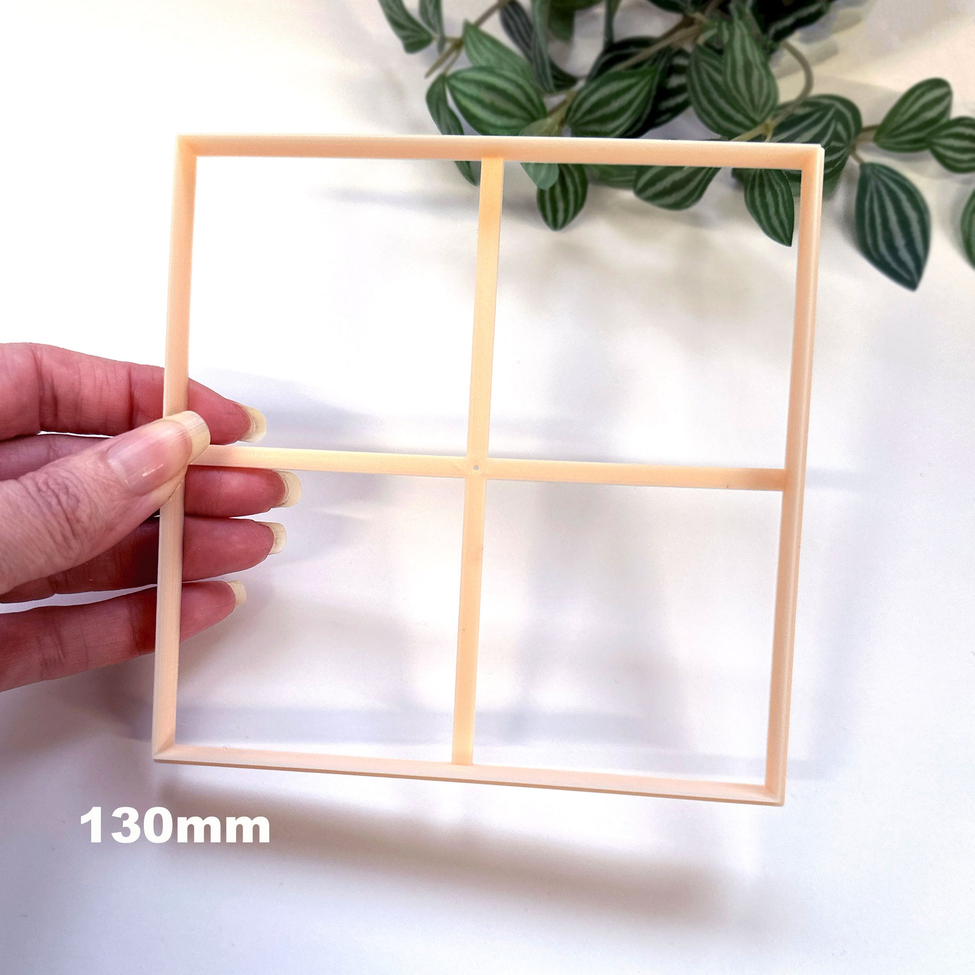 Large square clay cutter for larger clay crafts like pottery clocks, coasters, tricket plates, jewellery trays etc. The cutter is being held in hand tilted with leafs on a white background. 130mm is written.
