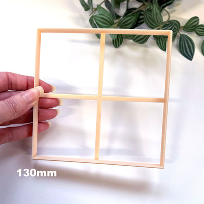 Large square clay cutter for larger clay crafts like pottery clocks, coasters, tricket plates, jewellery trays etc. The cutter is being held in hand tilted with leafs on a white background. 130mm is written.